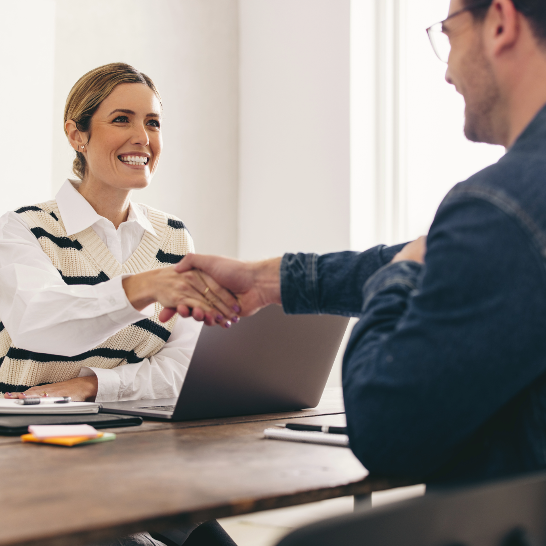 Woman and man shaking hands across a table for an interview.