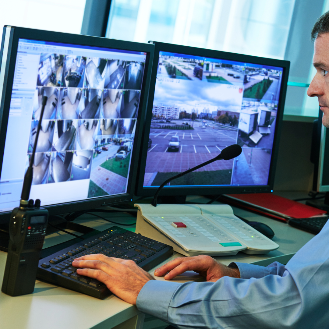 A man sitting at his desk, watching video surveillance footage on his computers.
