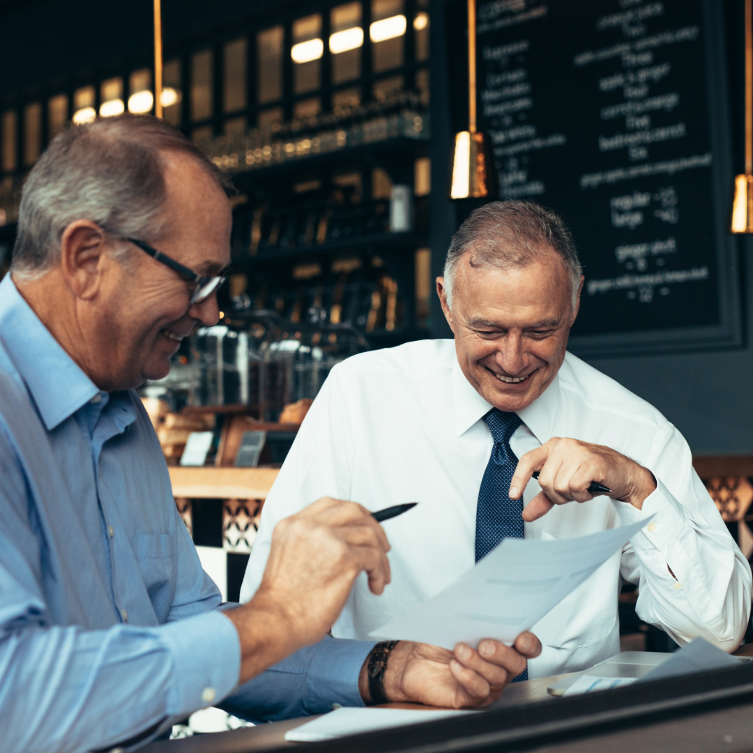 Two men sitting at a table in a restaurant, looking at reports together.
