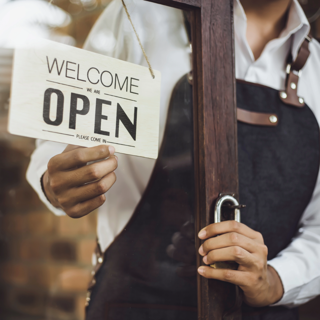 QSR employee wearing an apron flipping the sign on the restaurant door to Open.