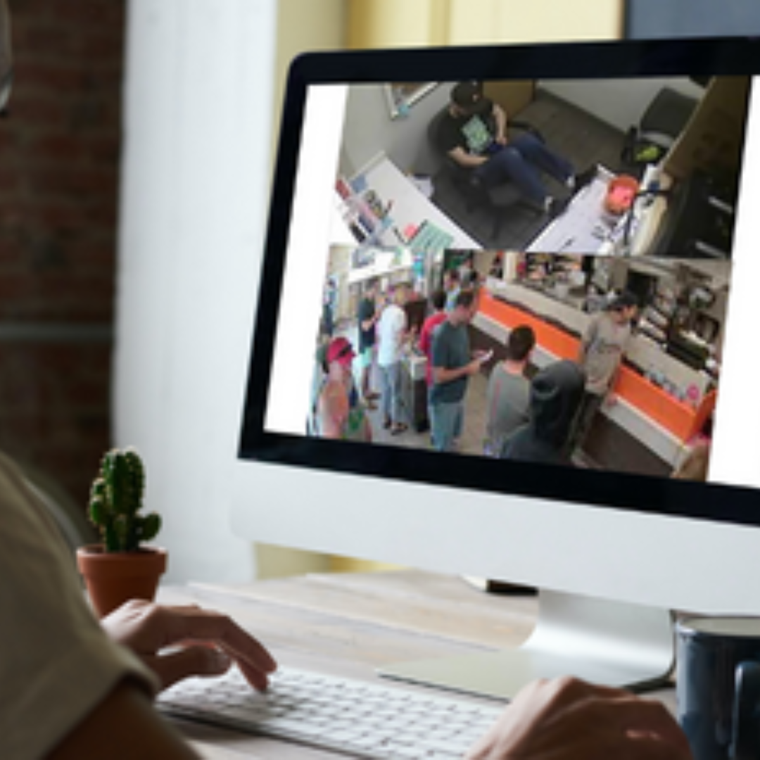 Person looking at a computer screen, showing a camera view of a QSR employee in the back on their phone while a long line of customers is gathering in the front.