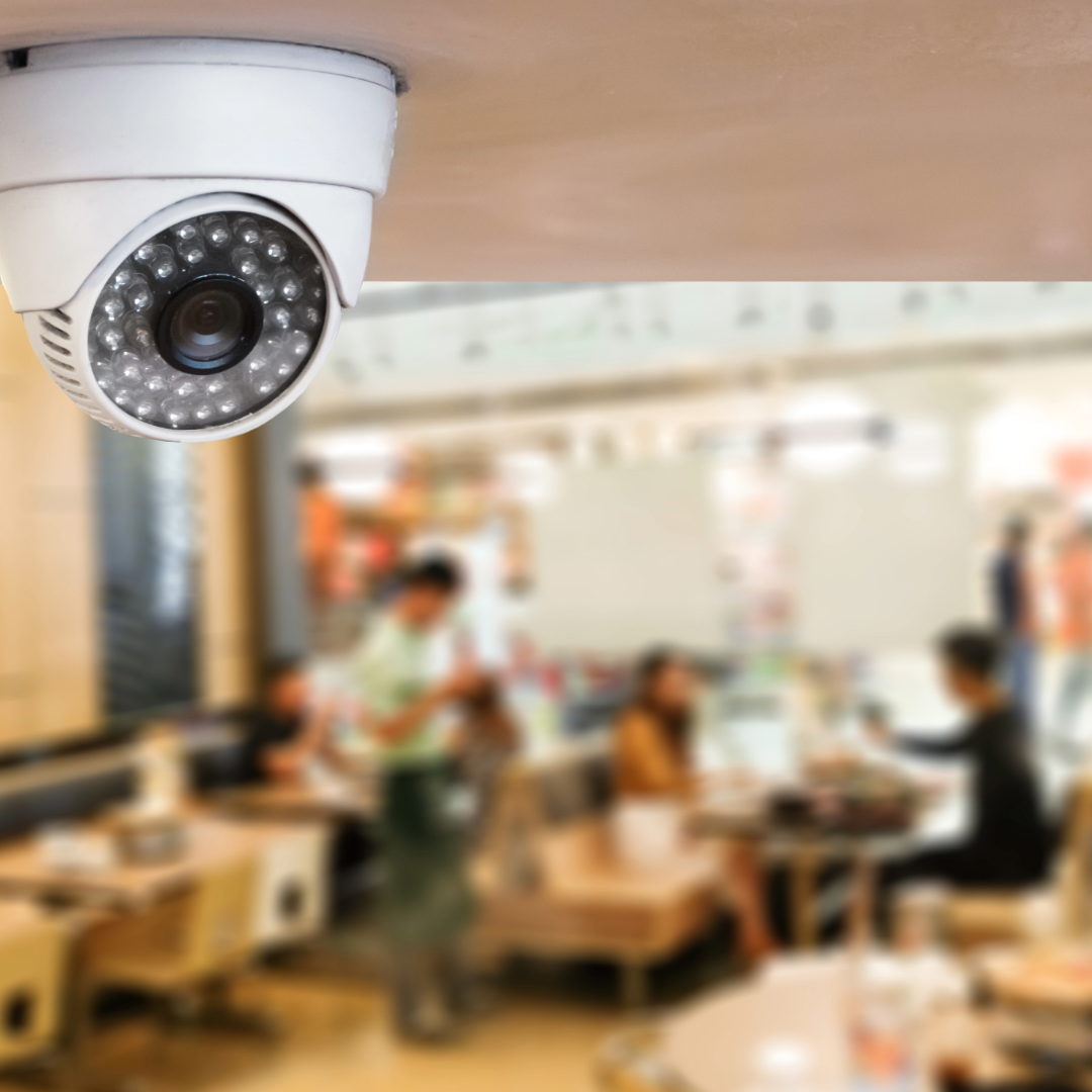 A surveillance camera in a quick-service restaurant. People and tables are in the background.