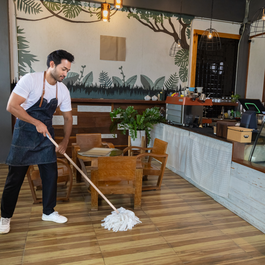 Man in apron mopping floor of cafe.