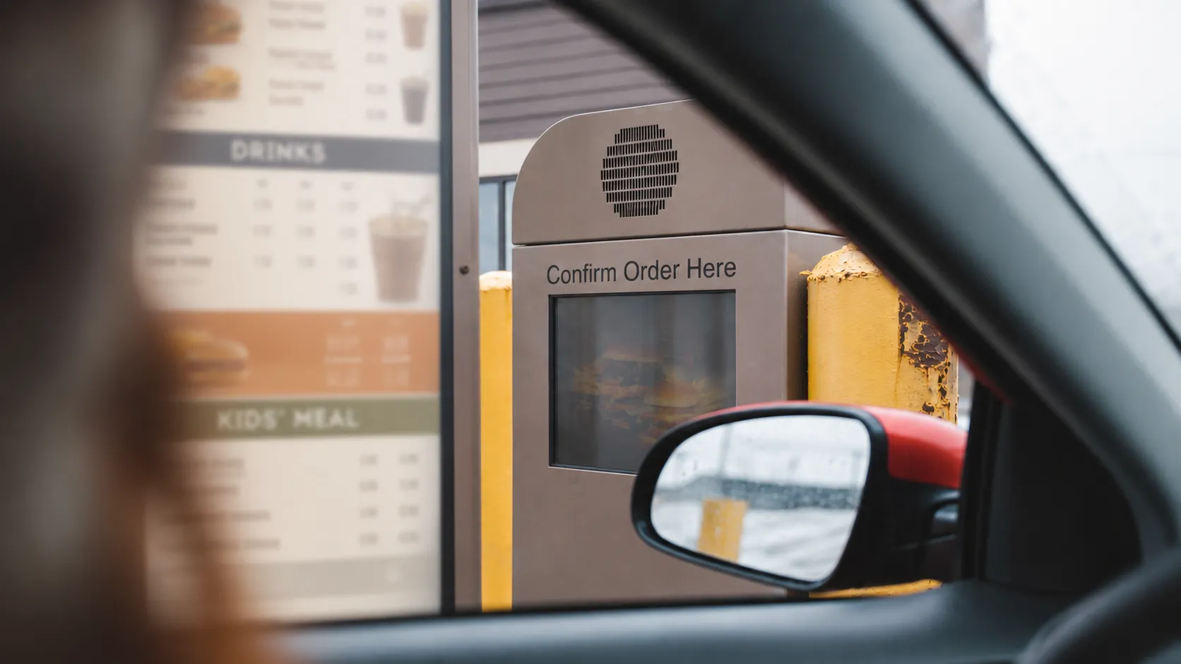 Driver view from inside a vehicle looking at a fast-food drive-thru menu board and order confirmation speaker.